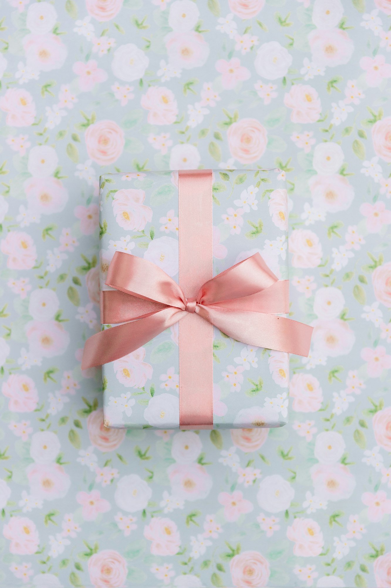 Un cadeau emballé de papier fleuri et noué d’un ruban rose