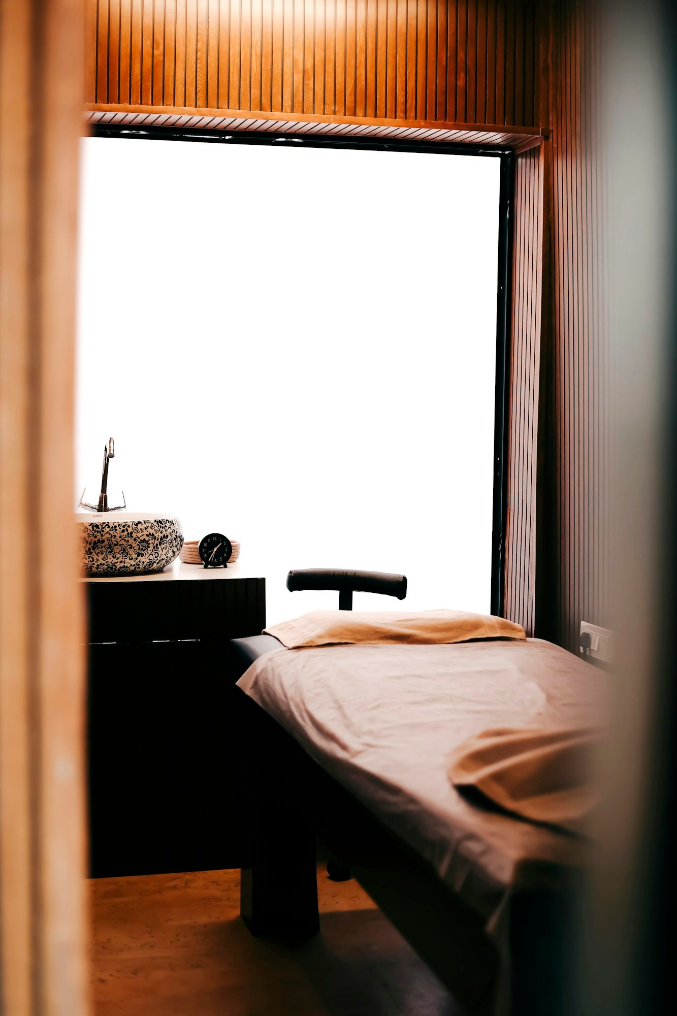 Une cabine de soin : table de massage, linge rose poudré et grande fenêtre