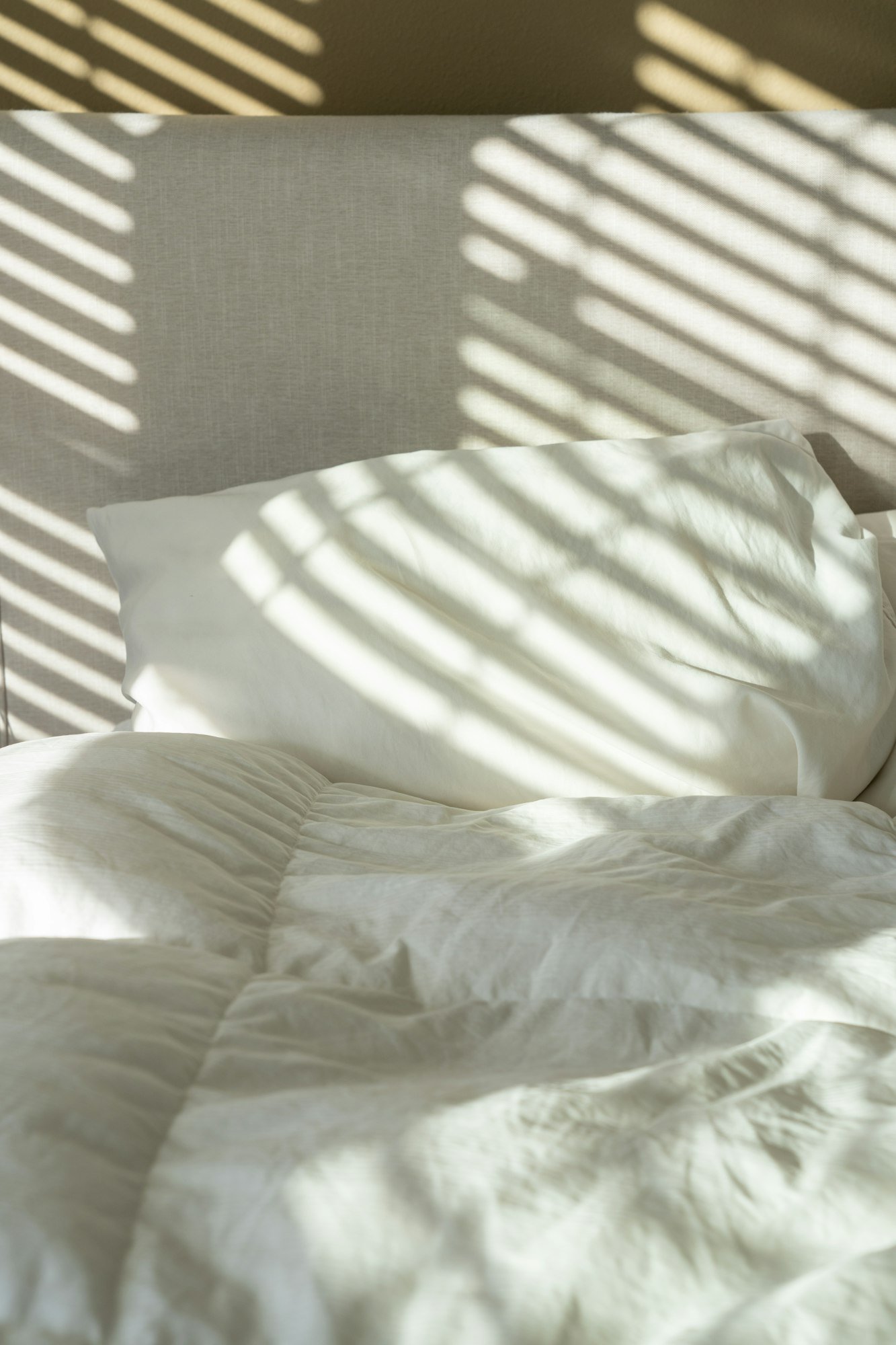 Un lit aux draps blancs, rayé par la lumière des persiennes