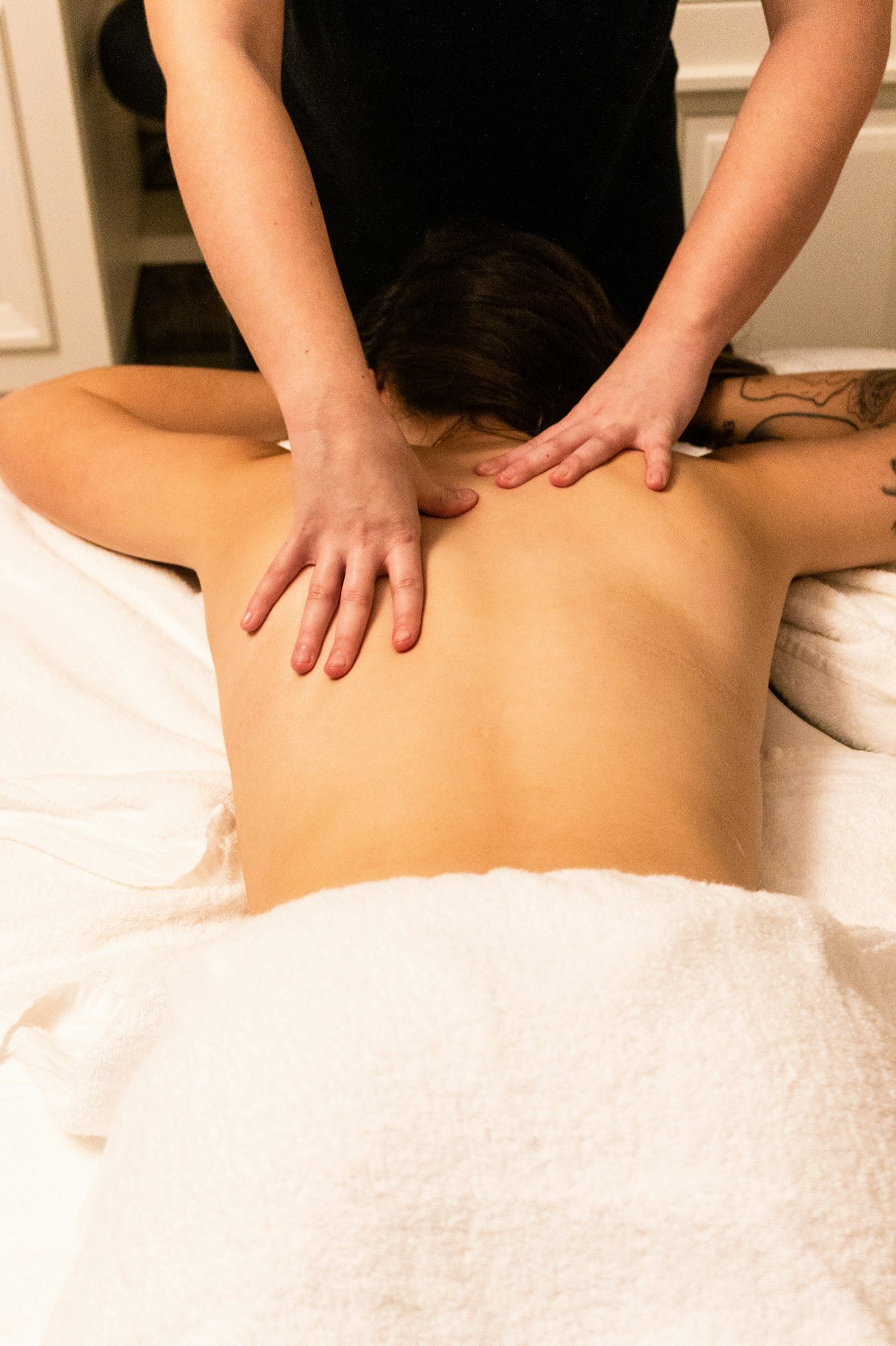 Une cliente allongée sous une serviette blanche, pendant un massage des épaules
